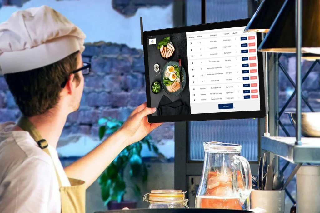 Chef using a tablet to manage kitchen orders in a restaurant setting.